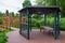 Iron gazebo with a roof for relaxing on a wooden bench in the backyard with a vertical pergola.