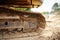 Iron track yellow excavator standing on sand with visible trees