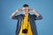 Irritated male traveler with photo camera covering his ears with fingers on blue studio background