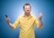 Irritated young man talks on the phone over blue background, dresses in yellow shirt. Annoyed guy talking. Stressed person using