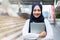 Islamic student or working woman standing with her arms crossed holding her laptop, smiling confidently