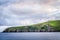 Island with tall cliffs, green fields with grazing cattle and beautiful pastel cloudy sky