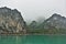 Islands in Halong Bay in the fog. Calm emerald water and a narrow strip of sand on the shore.