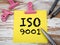 Iso 9001 standard for quality. Yellow sheet of paper and pencils on a wooden table