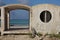 Isolated abandoned concrete beach first aid station with a cross on the wall, standing in white sand with the ocean, blue sky,