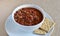 Isolated bowl of chili soup with whole wheat saltine crackers.