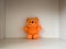 Isolated children`s toy against a light wood texture background, an old orange teddy bear from childhood