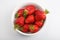 Isolated close up top view shot of a bunch of whole vibrant red strawberries in a bowl on a white background