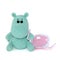 Isolated crocheted amigurumi toy small turquoise hippo with a sad surprised look sits, holds a pink-white cap in its paw