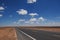 Isolated desert highway stretching out into the horizon, surrounded by lush clouds