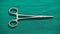 Isolated Hemostatic Forceps scissor on a green-clothed tabletop