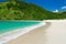 Isolated lonesome lagoon with turquoise sea, white surf in shallow water, white soft sand and lush green hill