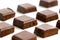 An isolated pile of milk chocolate slab blocks broken up and laid out in rows on a white background