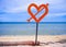 Isolated post signal with red love heart and arrow at beach on a blue sea and sky background in Valentines day and romance concept
