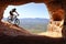 ISOLATED RIDER WITH HELMET AND BACKPACK DESCENDING IN A MOUNTAIN BIKE TOWARDS THE ENTRANCE OF A CAVE IN SUMMER