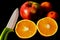 Isolated ripe orange fruit cut in half. red apple and small tangerines. White porcelain knife blade. Black background.