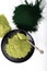 An isolated tablespoon of dried organic wheat grass and spirulina powder, on white rustic background