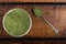 An isolated tablespoon of dried organic wheat grass and spirulina powder, on white rustic background