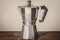 Isolated used vintage moka pot on a white background standing on a retro wooden table.