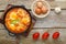 Israeli fried eggs shakshuka with cheese in a frying pan near eggs and tomatoes.