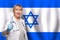 Israeli smiling mature doctor woman holding stethoscope on flag of Israel background