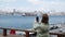 ISTANBUL, TURKEY - MAY, 2021: tourist woman photographing mobile selfie on Bosphorus embankment. Boats and ships sailing