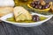Italian Bread with Oil for Dipping with Herbs & Spices. Olive oil sauce in white bowl & Greek olives on wood background