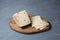 Italian Caciotta cheese with black pepper on wooden cutting board. Grey background, selective focus, copy space