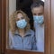 Italian couple with protective mask at the window looks out with a dejected expression because of the quarantine from covid-19