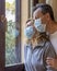 Italian couple with protective mask at the window looks out with a dejected expression because of the quarantine from covid-19