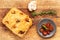 Italian focaccia with confit garlic cloves and rosemary, alongside tomatoes,  garlic bulb and rosemary twig on a wood board