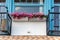 Italian house with blue wooden window frames and balcony with potted flowers, geraniums