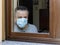 Italian man with protective mask, forced to stay at home due to coronavirus covid-19, disconsolate looks out the window