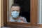 Italian man with protective mask, forced to stay at home due to coronavirus covid-19, disconsolate looks out the window