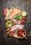 Italian meat plate with various antipasti, ciabatta bread, pesto and ham on rustic wooden background, top view