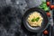 Italian pasta Orzo. Recipe with cream sauce, bacon and Basil. Prepared risoni. Black wooden background. Top view. Copy space