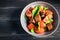 Italian salad of sliced tomatoes, basil leaves, olives, large pieces of croutons. In a deep plate, on a dark background