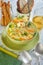Italian soup with spaghetti, carrots, lemon, parsley and pieces of chicken in a green plate, on a table with napkins, spoons of