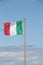 Italian tricolor flag fluttering in the wind, the flag on a concrete pole against the background of a blue sky