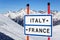 Italy or France choice to ski or snowboard. Information sign on winter mountain peaks under blue sky background