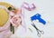 Items to decorate a bonnet includes a straw hat, vintage scissors, silk roses and a glue gun on a rustic wooden background