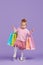 Ittle child girl on a purple background holding shopping bags, package.