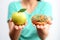 Itâ€™s hard to choose healthy food concept, with woman hand holding an green apple and a calorie bomb donut