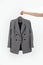 Jacket in a classic gray check on a hanger. A hand holds a jacket on a hanger. Vertical photo. Unrecognizable person. Light