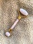 Jade stone roller made of pink quartz on plush beige background