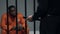 Jail guard with baton looking at afro-american prisoner in cell, harassment