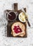 Jam, butter, toast bread on wooden cutting board on a light background.