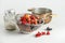Jam ingredients: various fruits and berries in colander with cooking pot and sugar in glass jar standing on white background