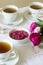 Jam from the petals of the Damascus rose, a cup of green tea and a vase of roses on a light table. Rustic style.