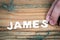 JAMES. Name of men and boys. White letters of the alphabet on a wooden background